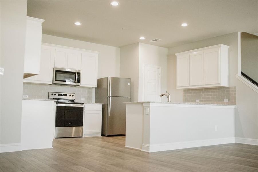 Kitchen with white cabinets, decorative backsplash, and appliances with stainless steel finishes