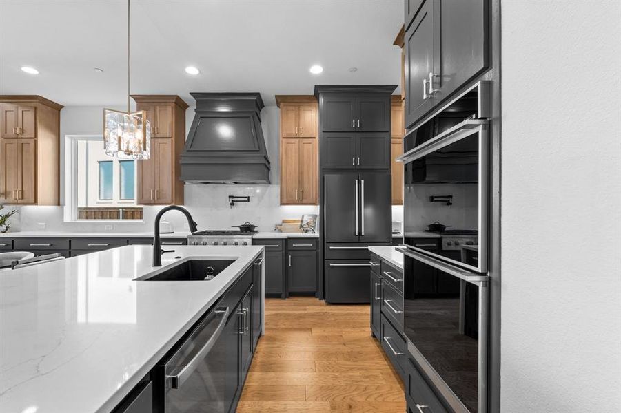 Kitchen featuring double oven, light wood-type flooring, high end black fridge, pendant lighting, and custom range hood Kitchen featuring double oven, light wood-type flooring, high end black fridge, pendant lighting, and custom range hood