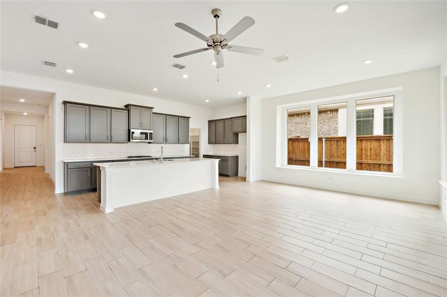 Kitchen with ceiling fan, decorative backsplash, sink, and a kitchen island with sink