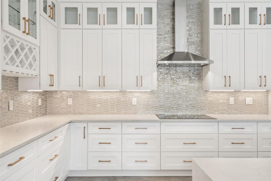 Kitchen featuring light stone countertops, wall chimney range hood, glass insert cabinets, white cabinetry, and decorative backsplash Kitchen featuring light stone countertops, wall chimney range hood, glass insert cabinets, white cabinetry, and decorative backsplash
