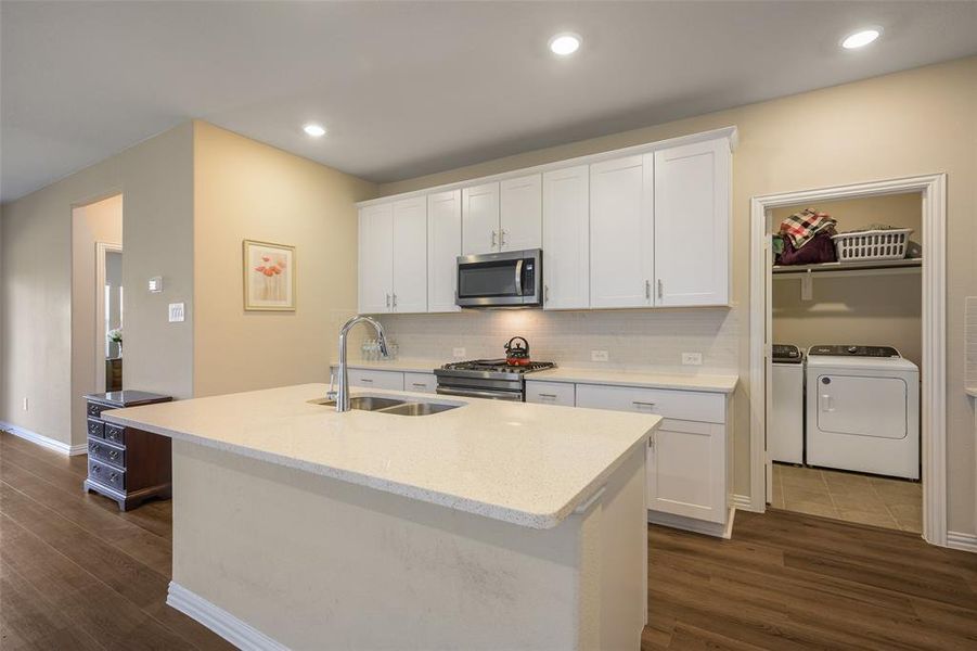 Kitchen featuring a central island with an undermount double-basin sink, stainless steel faucet, and light-toned countertop Kitchen featuring a central island with an undermount double-basin sink, stainless steel faucet, and light-toned countertop