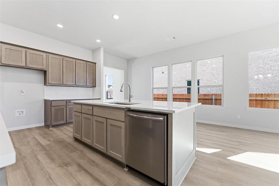 Kitchen featuring stainless steel dishwasher, recessed lighting, light wood-style floors, a kitchen island with sink, and light stone countertops