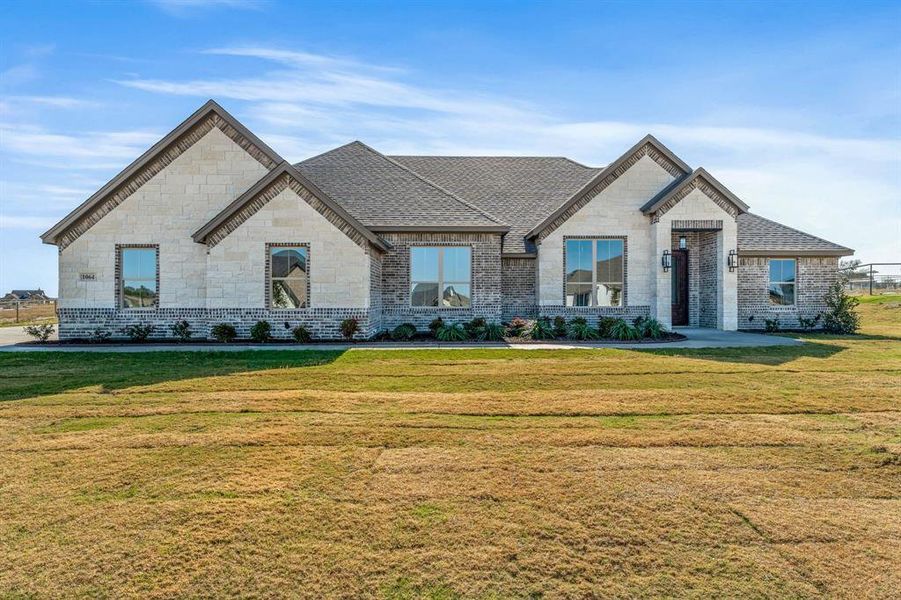 French country inspired facade featuring a front lawn, roof with shingles, and stone siding