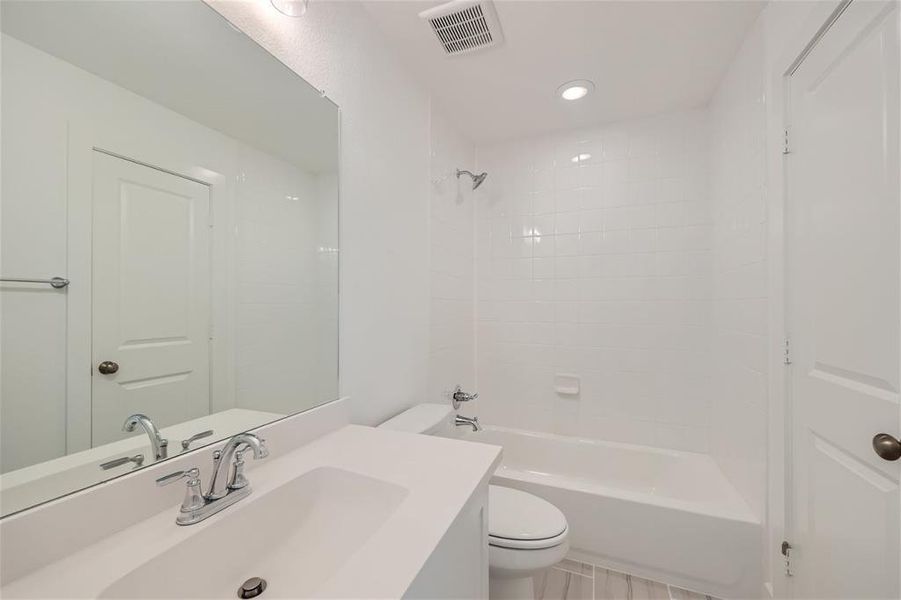 Full bathroom with vanity, tile patterned floors, tiled shower / bath combo, and toilet