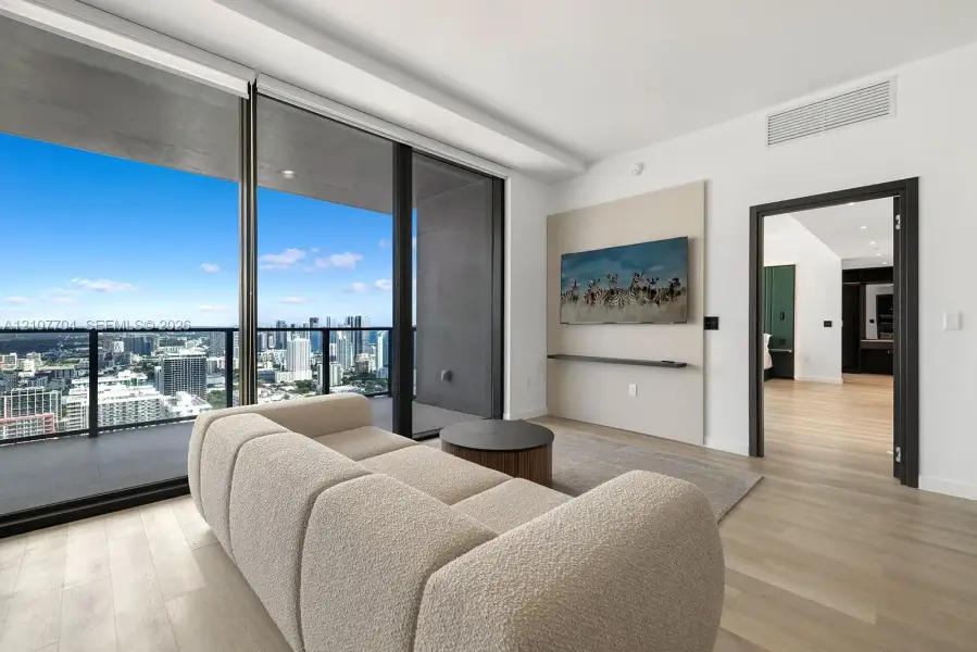 Floor-to-ceiling sliding glass doors, private balcony with metal railing, light wood-finish flooring, and a built-in wall panel with integrated shelf
