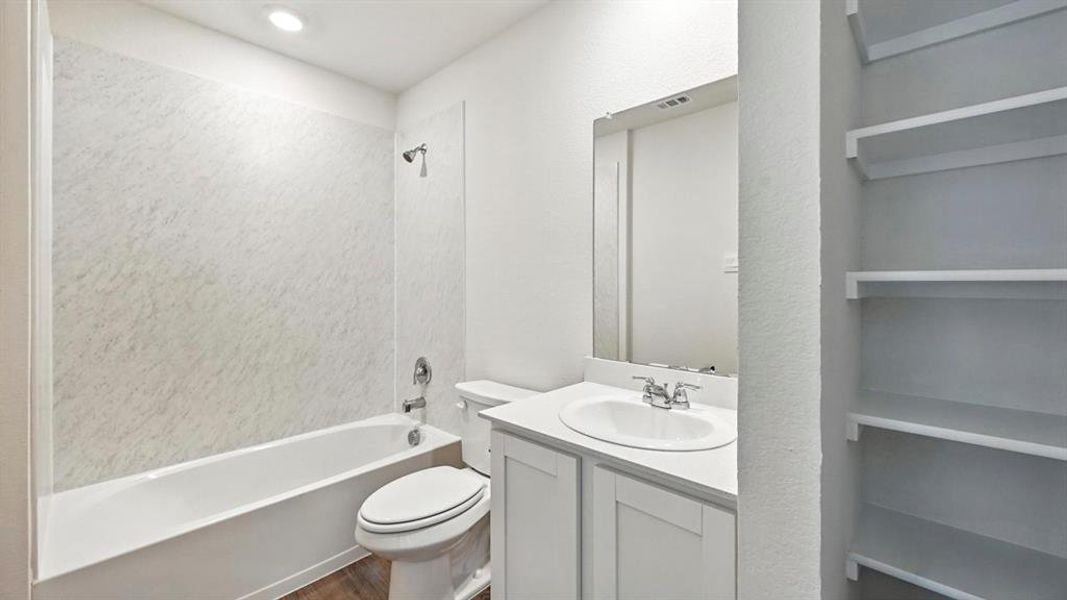 Bathroom featuring a white bathtub with a textured surround, a vanity with a white countertop and integrated sink, a large mirror, and built-in shelving