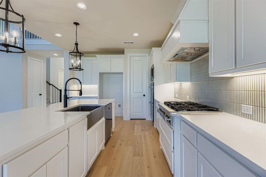Kitchen featuring white cabinets, recessed lighting, decorative backsplash, light wood-style floors, and premium range hood
