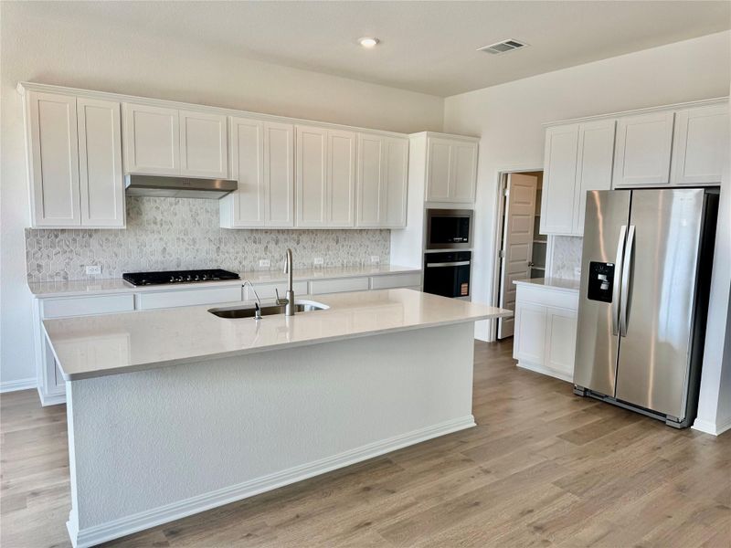 Kitchen featuring stainless steel appliances, white cabinets, decorative backsplash, light stone countertops, and light wood-style floors
