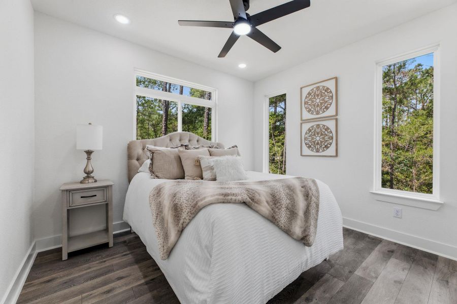 A tranquil bedroom retreat features a ceiling fan and ample natural light from surrounding tree views.