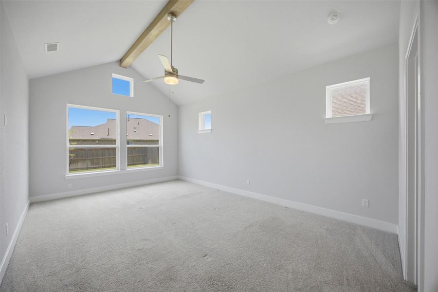 A spacious chamber with lofty vaulted ceilings, showcasing an exposed beam and a ceiling fan, illuminated by multiple windows.