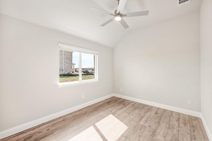 Empty bedroom with light wood floors, vaulted ceiling, ceiling fan, and single window Empty bedroom with light wood floors, vaulted ceiling, ceiling fan, and single window