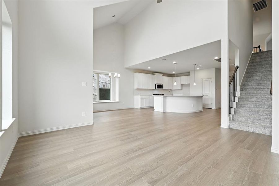 Unfurnished living room featuring high vaulted ceiling, stairs, light wood-style flooring, and a chandelier