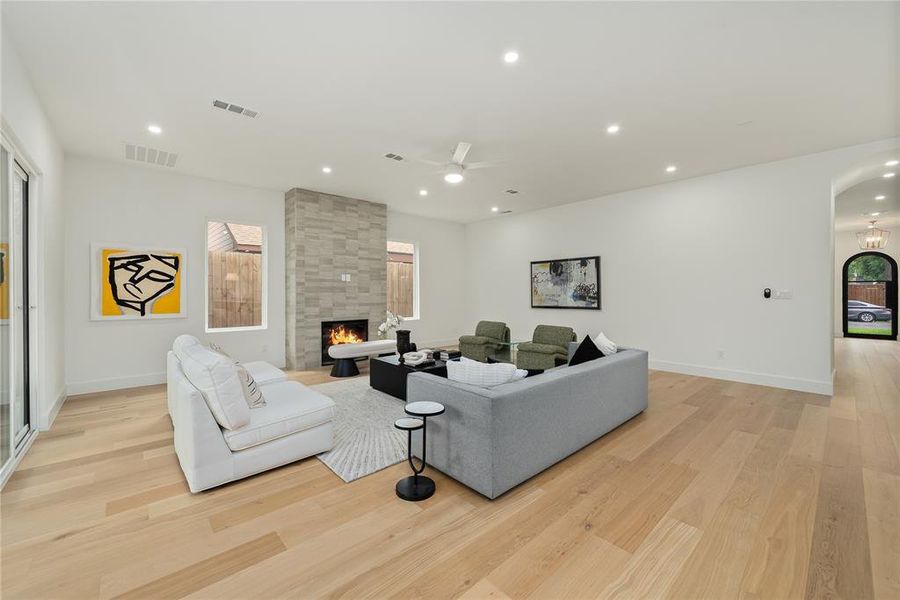 This inviting living space features light-toned hardwood flooring, a stone-clad fireplace, and recessed lighting