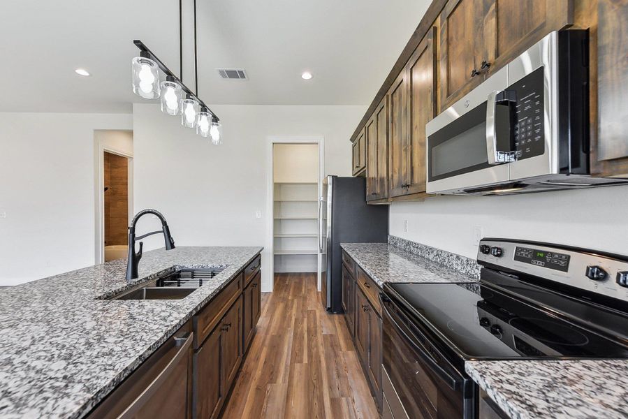 Kitchen featuring visible vents, appliances with stainless steel finishes, wood finished floors, hanging light fixtures, and a sink Kitchen featuring visible vents, appliances with stainless steel finishes, wood finished floors, hanging light fixtures, and a sink