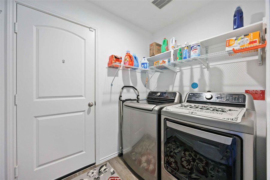 Bright laundry room featuring ample storage shelving and hookups for full-size washer and dryer Bright laundry room featuring ample storage shelving and hookups for full-size washer and dryer
