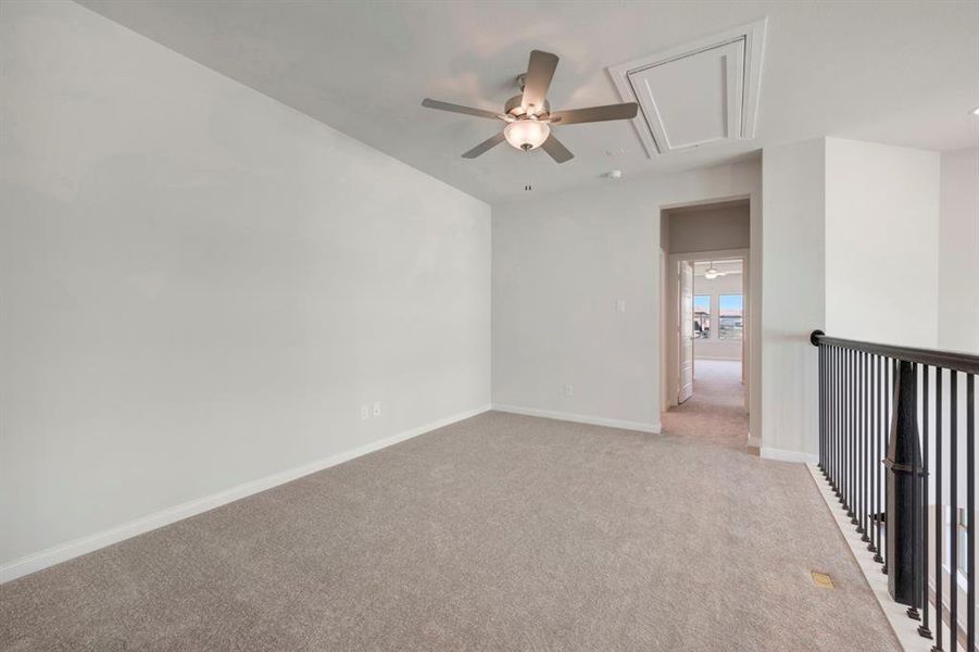 Carpeted empty room featuring attic access and ceiling fan