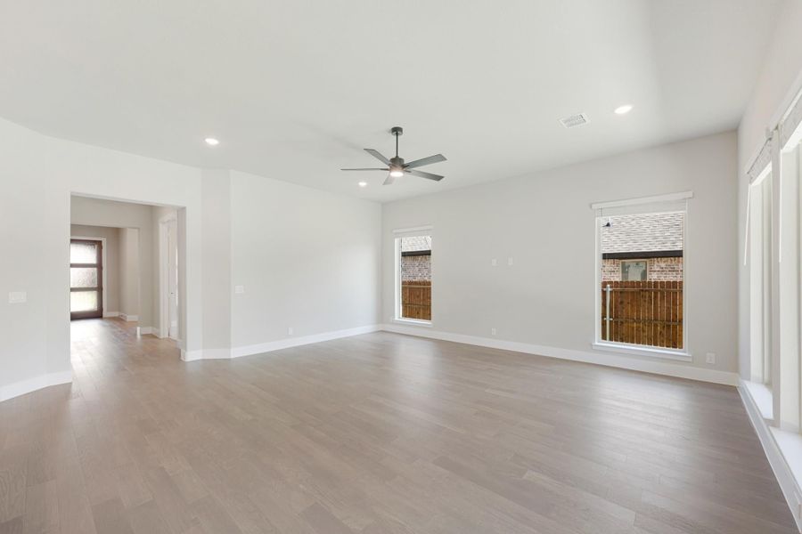Empty living room with light wood floors, ceiling fan, and two windows with backyard view