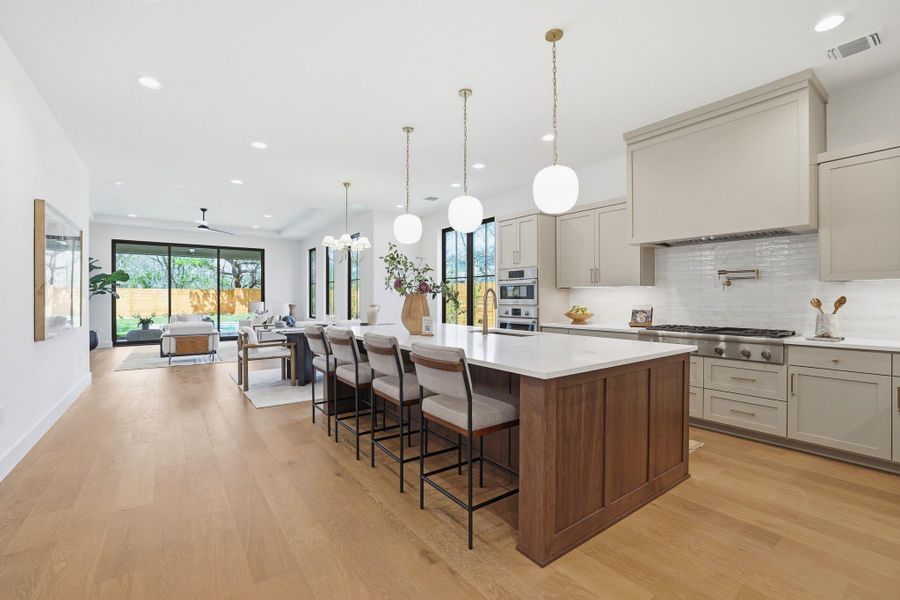 Kitchen featuring two tone cabinets, a large island, light wood-style floors, a breakfast bar, and backsplash