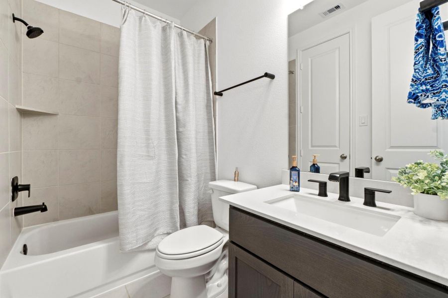 This bathroom features a modern design with a sleek vanity and black fixtures. It includes a bathtub with a tiled shower, neutral tones, and ample lighting, creating a fresh and welcoming atmosphere.