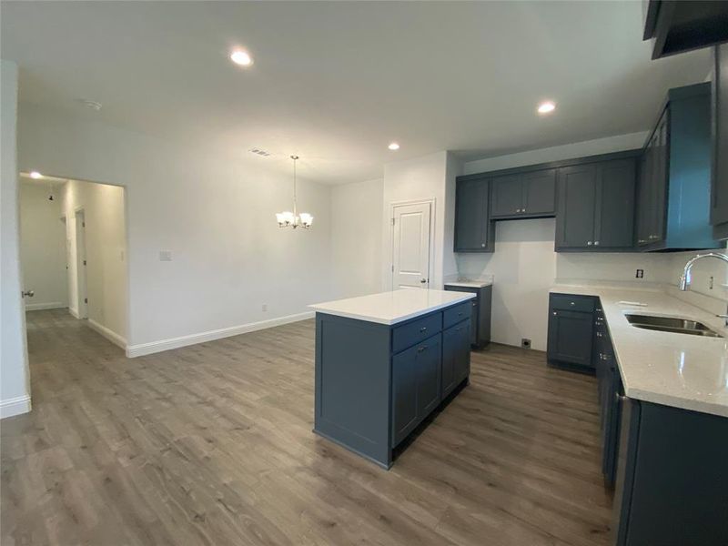 Kitchen with recessed lighting, light stone countertops, dark wood-type flooring, a center island, and a chandelier Kitchen with recessed lighting, light stone countertops, dark wood-type flooring, a center island, and a chandelier