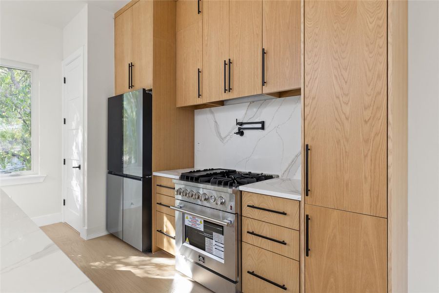Warm wood cabinetry pairs with slab stone backsplashes and professional gas cooking appliances.