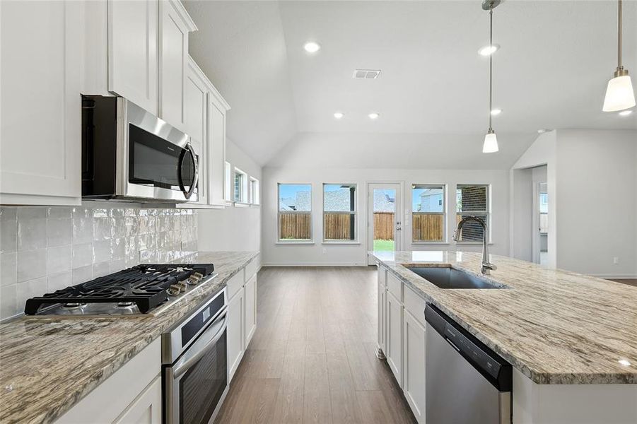 Kitchen with white cabinets, vaulted ceiling, stainless steel appliances, recessed lighting, and light stone counters Kitchen with white cabinets, vaulted ceiling, stainless steel appliances, recessed lighting, and light stone counters