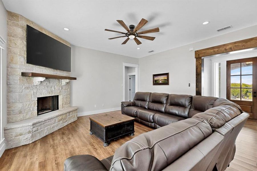 Living area featuring light wood finished floors, ceiling fan, a stone fireplace, and recessed lighting