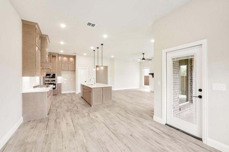 Open-concept kitchen and living area with tan cabinets, center island, pendant lights, and light wood floors
