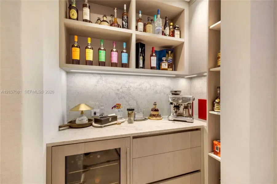 Custom built-in cabinetry with integrated lighting, stone-surface countertop, stone backsplash, and built-in under-counter beverage refrigerator Custom built-in cabinetry with integrated lighting, stone-surface countertop, stone backsplash, and built-in under-counter beverage refrigerator