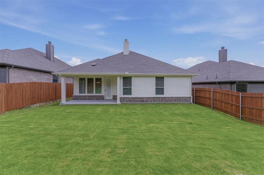 Expansive rear lawn featuring a covered concrete patio with white columns, horizontal siding, stone veneer accents, and a privacy fence