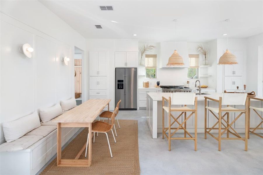 Kitchen with a breakfast bar area, appliances with stainless steel finishes, an island with sink, white cabinetry, and pendant lighting Kitchen with a breakfast bar area, appliances with stainless steel finishes, an island with sink, white cabinetry, and pendant lighting