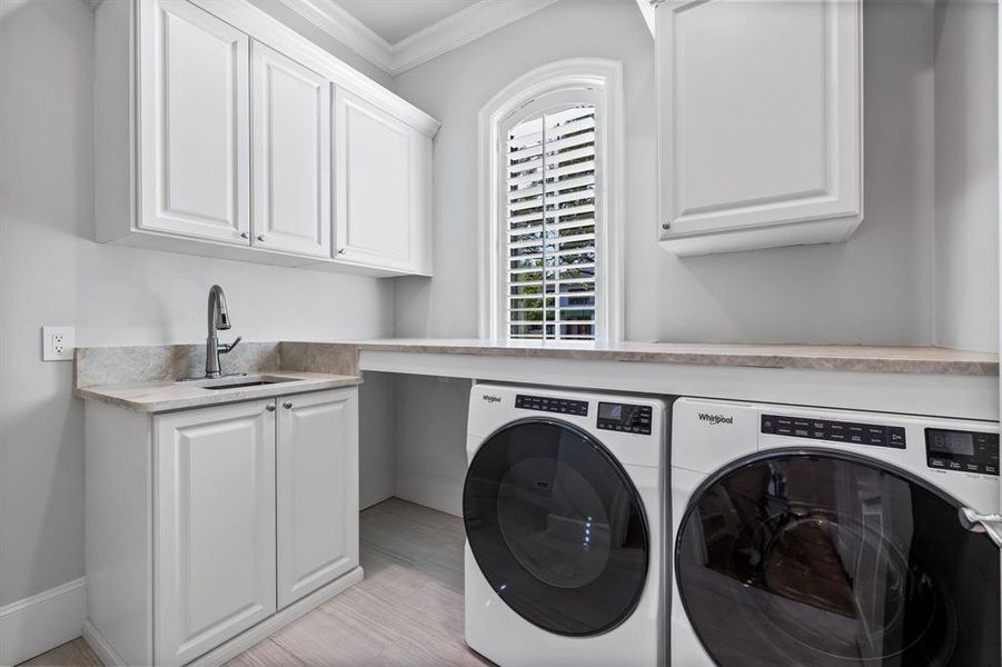 Washroom featuring sink, ornamental molding, light hardwood / wood-style flooring, cabinets, and washing machine and clothes dryer