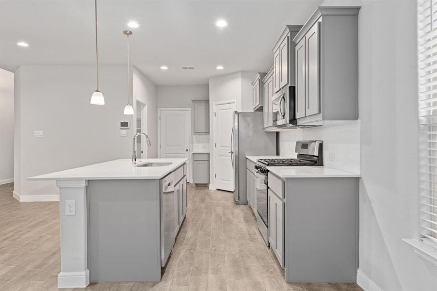 Kitchen with appliances with stainless steel finishes, decorative light fixtures, an island with sink, sink, and light wood-type flooring