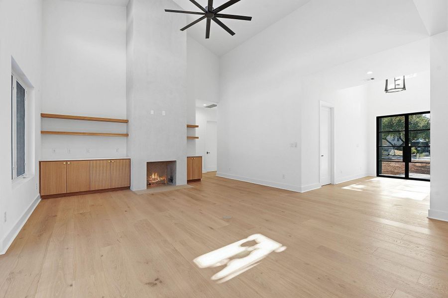 Towering ceilings and light hardwood floors anchor this airy living space with a plaster fireplace.