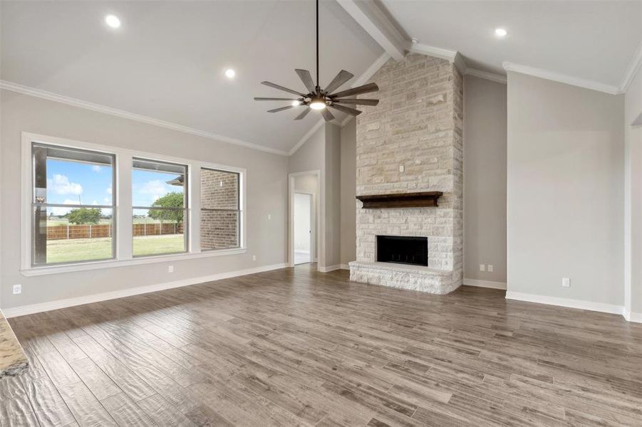 Unfurnished living room featuring ceiling fan, ornamental molding, lofted ceiling with beams, a fireplace, and hardwood / wood-style floors