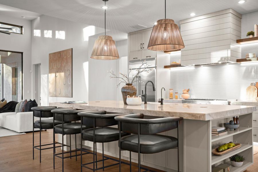 Kitchen featuring open shelves, an island with sink, hanging light fixtures, light stone counters, and light wood-style flooring