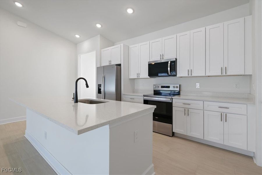 Kitchen featuring stainless steel appliances, light stone counters, a center island with sink, white cabinetry, and light wood finished floors Kitchen featuring stainless steel appliances, light stone counters, a center island with sink, white cabinetry, and light wood finished floors