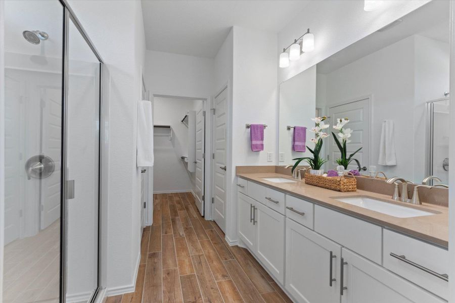 Full bath featuring a shower stall, double vanity, quartz countertops a walk in closet, and light wood tile finished floors