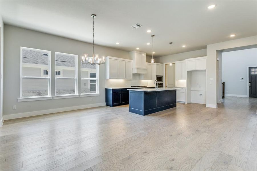 Kitchen with light hardwood / wood-style flooring, a center island with sink, white cabinets, and decorative light fixtures