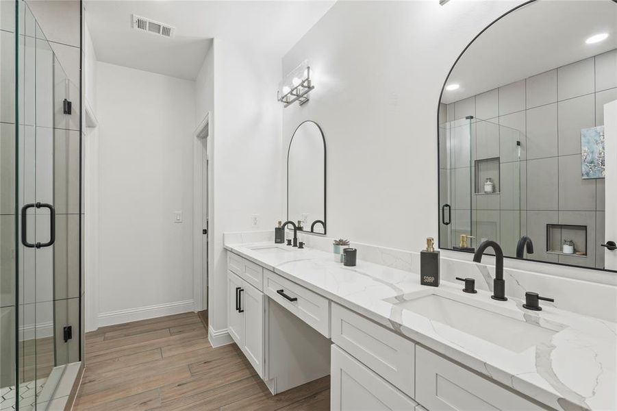 Bathroom with double vanity, a shower stall, and light wood-style flooring