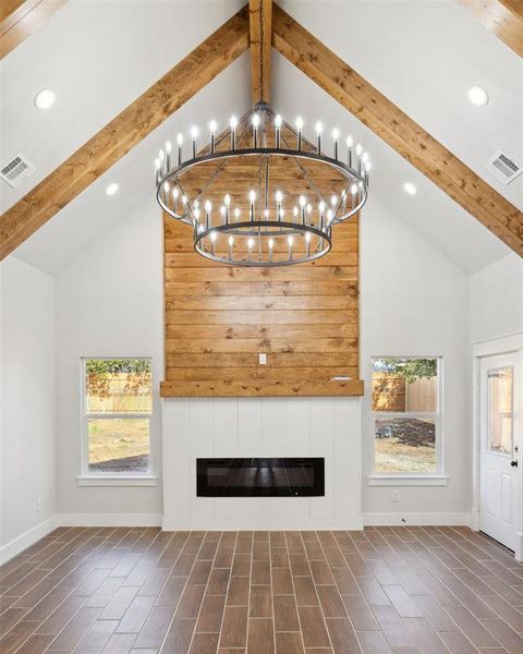 Unfurnished living room featuring a healthy amount of sunlight, beam ceiling, high vaulted ceiling, and a notable chandelier