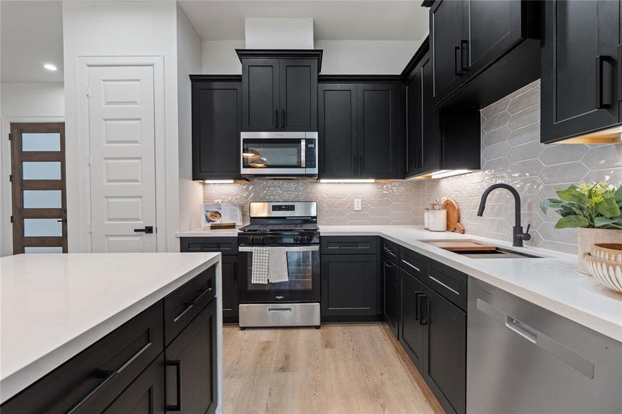 Sleek modern kitchen featuring elegant black cabinetry, stainless steel appliances, and a stylish hexagonal tile backsplash. Sleek modern kitchen featuring elegant black cabinetry, stainless steel appliances, and a stylish hexagonal tile backsplash.