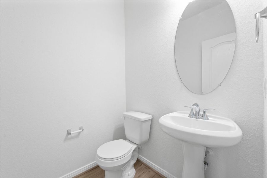 The powder room on the first floor includes a pedestal sink, mirror, and toilet to conveniently meet your needs.