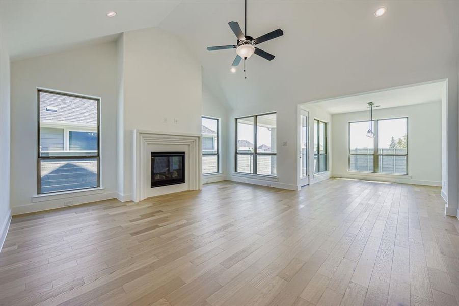 Unfurnished living room with high vaulted ceiling, a glass covered fireplace, light wood finished floors, recessed lighting, and ceiling fan Unfurnished living room with high vaulted ceiling, a glass covered fireplace, light wood finished floors, recessed lighting, and ceiling fan