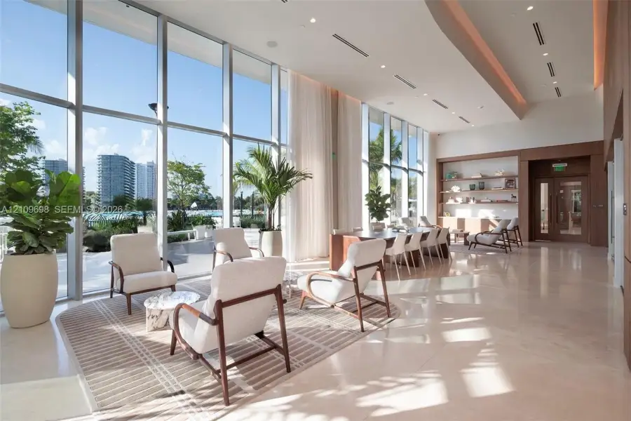 Floor-to-ceiling windows, high ceilings with recessed lighting, stone flooring, and built-in wood shelving