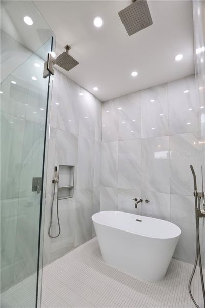 Indulge in a spa-like experience with dual rainfall shower heads and separate handhelds for a personalized experience. Floor-to-ceiling tile in soft gray with warm, flowing swirls sets a tranquil tone. Indulge in a spa-like experience with dual rainfall shower heads and separate handhelds for a personalized experience. Floor-to-ceiling tile in soft gray with warm, flowing swirls sets a tranquil tone.