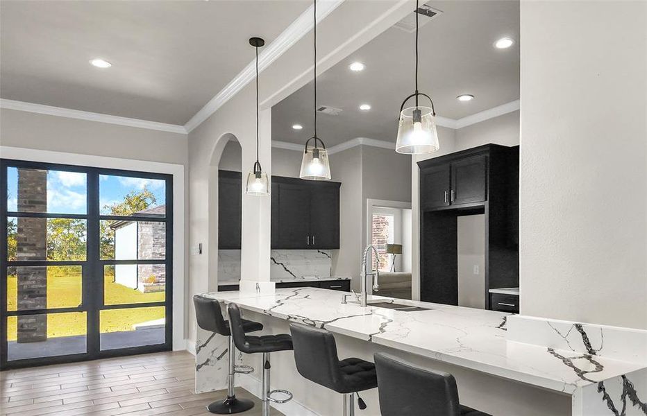Kitchen with light stone countertops, a breakfast bar area, an office area, wood finish floors, and decorative light fixtures