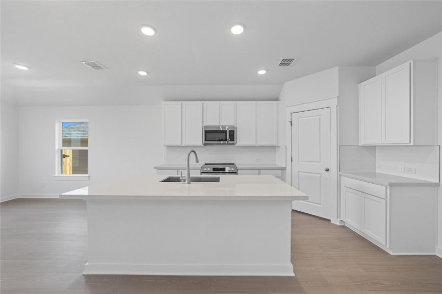 Kitchen featuring white cabinets, light wood finished floors, a kitchen island with sink, stainless steel appliances, and recessed lighting
