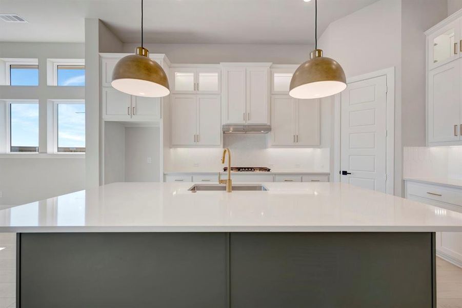 Two tone kitchen featuring dual tone cabinetry, glass fronted cabinets, pendant lighting, light stone countertops, and a center island with sink Two tone kitchen featuring dual tone cabinetry, glass fronted cabinets, pendant lighting, light stone countertops, and a center island with sink