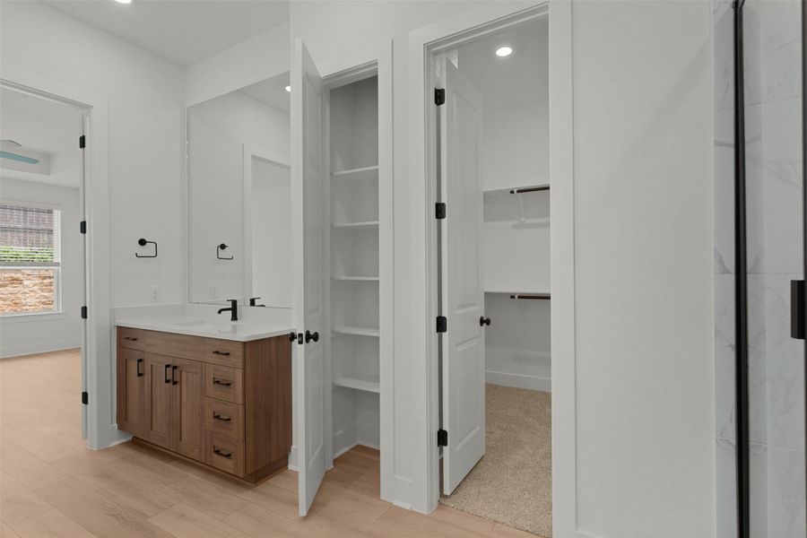 Bathroom vanity with wood-finish cabinetry, white countertop, and black fixtures Bathroom vanity with wood-finish cabinetry, white countertop, and black fixtures